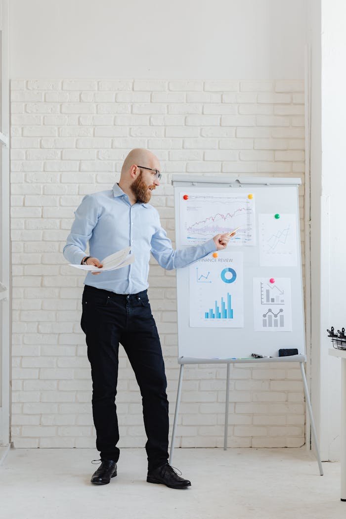 who-we-are A bearded man with eyeglasses explaining graphs on a flip chart in an office.